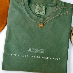 May include: A green t-shirt with the text "IT'S A GOOD DAY TO READ A BOOK" and a graphic of a stack of books.