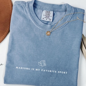 Show your love for the game with our “Mahjong Is My Favorite Sport” shirt! Perfect for Filipina moms, dads, and mahjong enthusiasts, this comfy Comfort Colors® tee is great for game nights or casual wear. A fun gift for players of American or traditional mahjong — stylish and spirited!