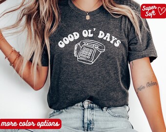 May include: Dark gray t-shirt with the words "GOOD OL' DAYS" and a white graphic of a retro telephone. The shirt has a crew neck and short sleeves. The words "Super Soft" are in a red box.