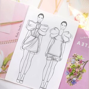 May include: A black and white line drawing of two fashion sketches. The sketches feature women wearing short dresses with large, dramatic sleeves. The text "Radu Andre" is written on the page.