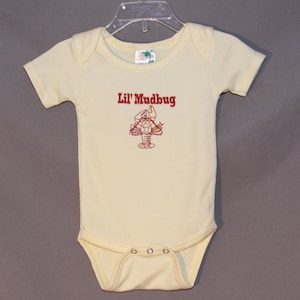 May include: A yellow baby onesie with short sleeves and a red embroidered lobster with the text "Lil' Mudbug" above it.