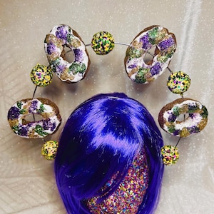 May include: A purple wig with a headband decorated with gold, green, and purple donuts and gold and green beads.