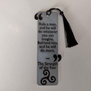 Peut inclure: Marque-page argent&eacute; avec un pompon noir. Le marque-page pr&eacute;sente une citation sur l'influence et l'amiti&eacute;, avec les mots "Rule a man...and he will do more." Le bas porte le texte "The Strength of the Few."