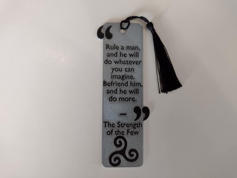 Peut inclure: Marque-page argent&eacute; avec un pompon noir. Le marque-page pr&eacute;sente une citation sur l'influence et l'amiti&eacute;, avec les mots "Rule a man...and he will do more." Le bas porte le texte "The Strength of the Few."