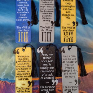 Peut inclure: Six marque-pages rectangulaires avec des citations et des d&eacute;tails de pompons noirs. Les marque-pages sont de diff&eacute;rentes couleurs, dont le bleu, le gris et le jaune. Chaque marque-page pr&eacute;sente une citation et un symbole.