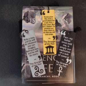 Peut inclure: Trois marque-pages d&eacute;coratifs avec des citations de "The Strength of the Few" sont pr&eacute;sent&eacute;s sur un livre. Les marque-pages sont jaunes, argent&eacute;s et noirs, chacun avec un design unique et un pompon. Le titre du livre est "ISLINGTON".