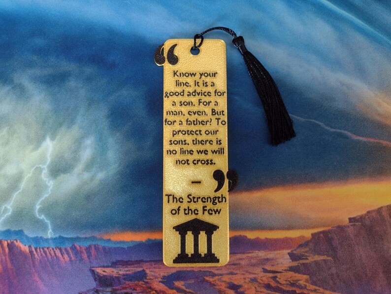 Peut inclure: Marque-page rectangulaire en bois avec un pompon noir. Le marque-page porte le texte grav&eacute; : "Know your line...The Strength of the Few" et un dessin de b&acirc;timent. Le fond est un paysage color&eacute;.