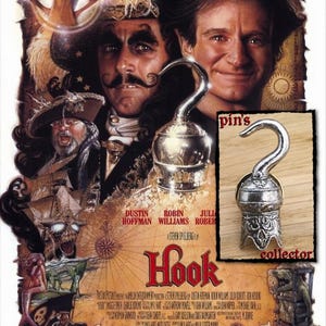 May include: A silver-toned metal pin shaped like a pirate hook, featuring an ornate, textured base with intricate detailing. The pin is displayed against a background of the movie poster for the film Hook, with the text pin's collector visible.