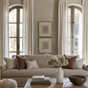 Puede incluir: Un sal&oacute;n de tonos neutros con un sof&aacute; beige adornado con varios cojines. Una mesa de centro de madera exhibe libros, un jarr&oacute;n blanco con flores secas y un cuenco de madera. Dos grabados bot&aacute;nicos enmarcados cuelgan de la pared.