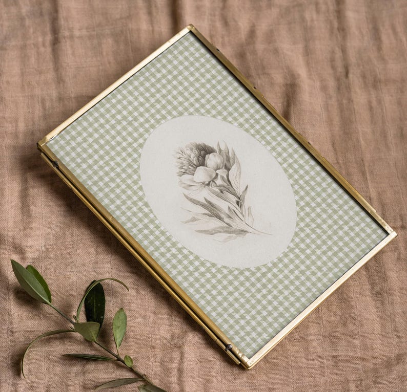 Pu&ograve; includere: Una cornice per foto in ottone con un motivo a quadri verdi e bianchi. La cornice contiene una stampa botanica in bianco e nero di un fiore.