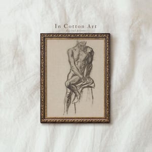 May include: A framed charcoal drawing of a seated figure. The artwork, with the text "In Cotton Art digital prints", depicts a detailed study of the human form in grey tones. The frame has an ornate gold and brown finish.