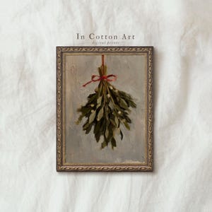 Puede incluir: Pintura enmarcada de muérdago atado con una cinta roja. La obra presenta hojas verdes con bayas blancas sobre un fondo gris. El marco es de color dorado detallado y ornamentado. El texto "In Cotton Art digital prints" está en la parte superior.