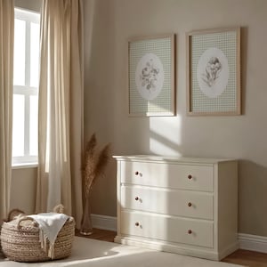 Pu&ograve; includere: Una cassettiera bianca con tre cassetti e pomelli marroni. La cassettiera si trova in una stanza con pareti beige, modanature bianche e una finestra con tende beige. Due stampe incorniciate con motivi floreali sono appese al muro sopra la cassettiera.
