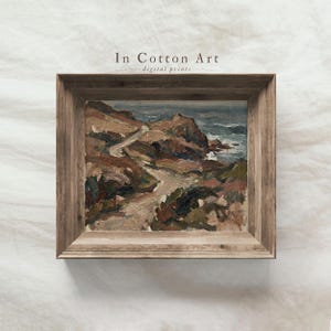 Pode incluir: Uma pintura de paisagem retangular numa moldura de madeira castanha envelhecida com uma cena costeira com falésias castanhas, um caminho sinuoso e ondas azuis. O texto In Cotton Art digital prints está centrado sobre a obra de arte.