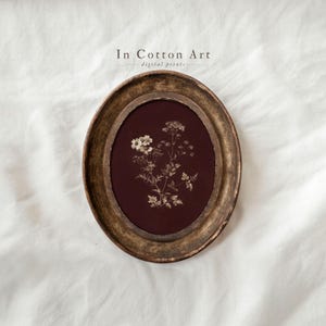 May include: An oval framed botanical print with a sepia-toned floral arrangement on a deep burgundy background. The frame is a distressed gold colour, and the text "In Cotton Art digital prints" is at the top.
