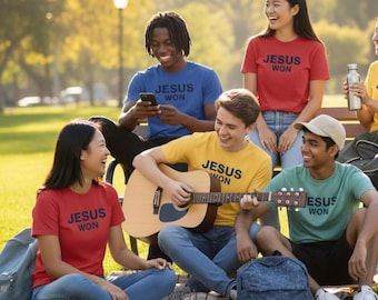 May include: A group of people wearing t-shirts with the text "JESUS WON" in a park setting. The shirts are red, blue, yellow, and green. One person is playing an acoustic guitar. The scene is outdoors on a sunny day.