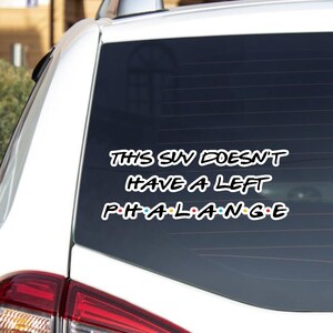 Puede incluir: Una pegatina blanca para la ventana del coche con el texto "THIS SIN DOESN'T HAVE A LEFT PHALANGE" en blanco. La palabra "PHALANGE" está en el estilo de la serie de televisión Friends, con cada letra de un color diferente.