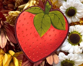 May include: A heart-shaped sticker featuring a red strawberry with green leaves. The sticker is surrounded by a colorful arrangement of yellow, white, and maroon flowers, creating a vibrant and eye-catching display.