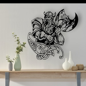 Puede incluir: Silueta en blanco y negro de un guerrero vikingo sosteniendo un hacha. El guerrero lleva un casco con cuernos y tiene una larga barba. El diseño está rodeado de intrincados nudos celtas.