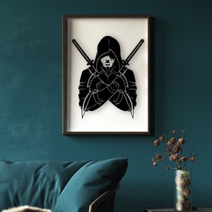 May include: A black and white illustration of a hooded figure with crossed swords behind them. The figure is in a dark, shadowy pose, with their face obscured by the hood. The image is framed in a black frame and hung on a teal wall.