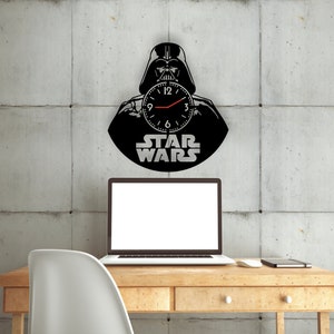 May include: A black and white wall clock featuring Darth Vader from Star Wars. The clock is shaped like a vinyl record and has a red second hand.