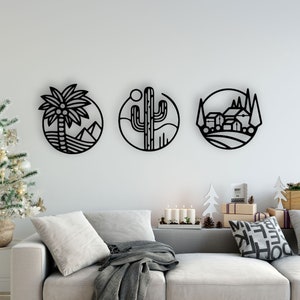 Puede incluir: Tres piezas de arte mural de metal negro que representan una palmera y montañas, un cactus y un paisaje rural. Cada diseño está encerrado en un marco circular. Se exhiben sobre un sofá gris con elementos decorativos.