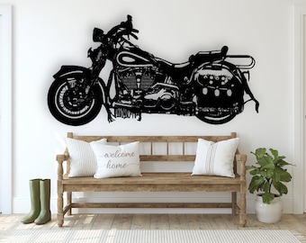 May include: Black silhouette of a motorcycle on a white wall. The motorcycle has a large front wheel and a smaller rear wheel. The motorcycle is decorated with fringe. The motorcycle is above a wooden bench with two pillows and a green plant.
