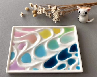 Pode incluir: Paleta de pintura de cerâmica branca com múltiplos poços em um design ondulado. Os poços estão cheios de diferentes cores de tinta, incluindo rosa, amarelo, verde, azul e turquesa.