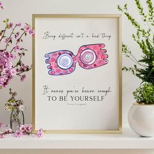 Puede incluir: Una impresi&oacute;n enmarcada en dorado con una ilustraci&oacute;n rosa y morada de un par de gafas. El texto de la impresi&oacute;n dice "Ser diferente no es algo malo. Significa que eres lo suficientemente valiente para SER T&Uacute; MISMO."