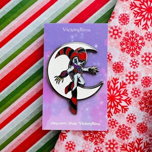 May include: A metal pin featuring a cartoon character standing on a crescent moon. The character has a red, black, white, and purple color scheme. The pin is on a purple card with the text "VictoryRina" and "etsy.com/shop/VictoryRina".
