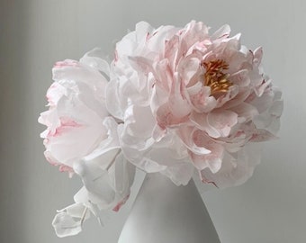 May include: A bouquet of white paper peonies with pink accents in a white ceramic vase with a geometric design.