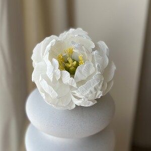 May include: A white ceramic vase with a stack of round, textured white ceramic pieces. A single white flower with a yellow center sits on top of the vase.