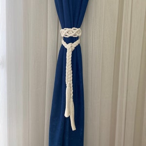 May include: A blue curtain with a white braided rope tieback. The tieback has a tassel at the end.