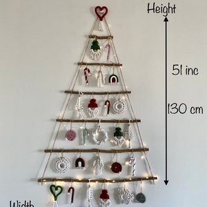 May include: A white wall with a macrame Christmas tree hanging on it. The tree is made of twine and has a variety of ornaments, including candy canes, stars, and hearts. The tree is 51 inches tall and 27 inches wide.