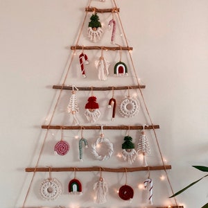 May include: A white wall with a Christmas tree made of branches and string. The tree is decorated with handmade ornaments, including gnomes, candy canes, hearts, and rainbows. The ornaments are made of yarn and fabric.