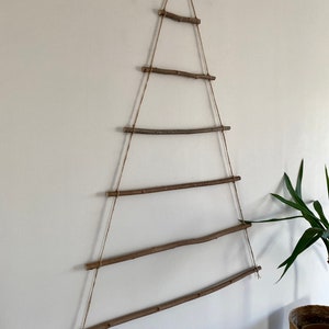 May include: A rustic wooden Christmas tree wall hanging made from natural branches and twine. The tree is made of six horizontal branches connected by twine, creating a triangular shape.