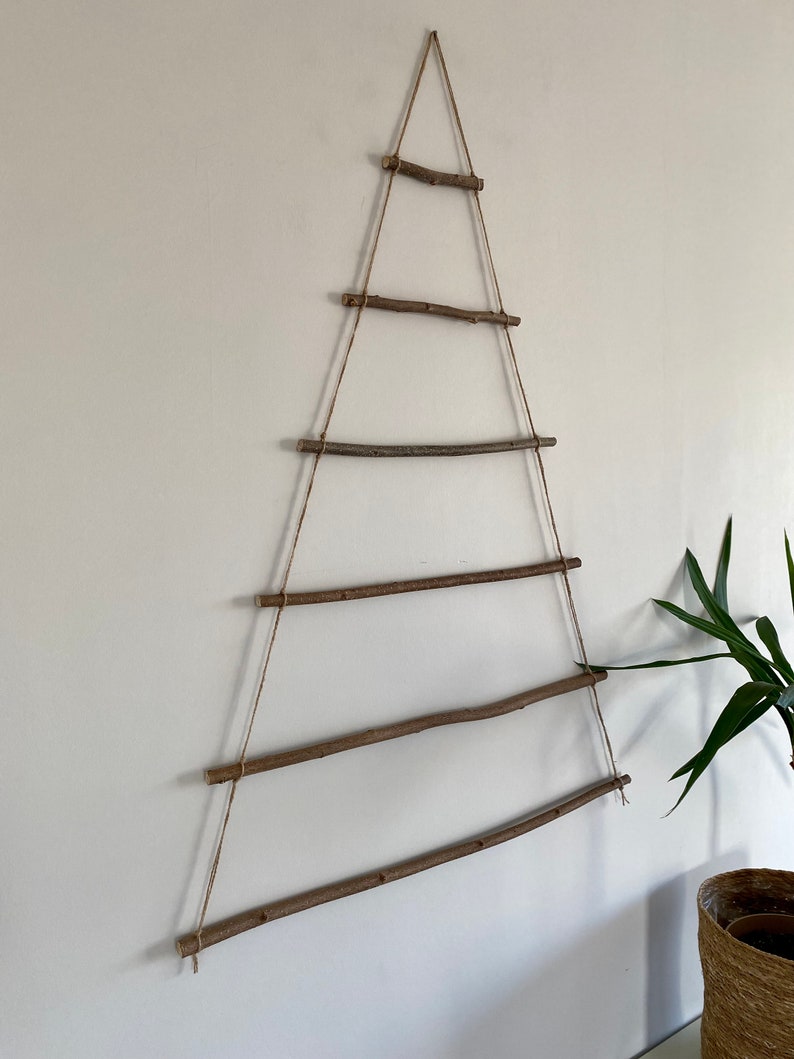 May include: A rustic wooden Christmas tree wall hanging made from natural branches and twine. The tree is made of six horizontal branches connected by twine, creating a triangular shape.