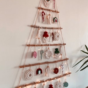 May include: A Christmas tree made of branches and twine with various handmade ornaments, including a heart, candy canes, a gnome, and a rainbow. The tree is decorated with white fairy lights.