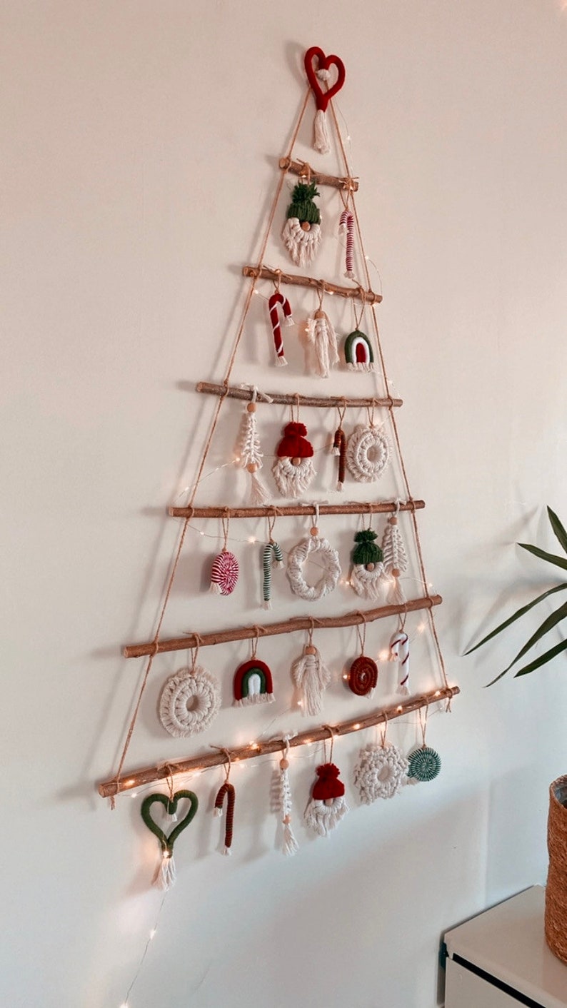 May include: A Christmas tree made of branches and twine with various handmade ornaments, including a heart, candy canes, a gnome, and a rainbow. The tree is decorated with white fairy lights.