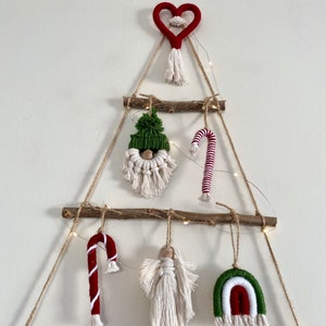 May include: A handmade Christmas tree wall hanging made of twine and wood. The tree is decorated with a red heart, a green and white gnome, a red and white candy cane, a white angel, and a green, white, and red rainbow.