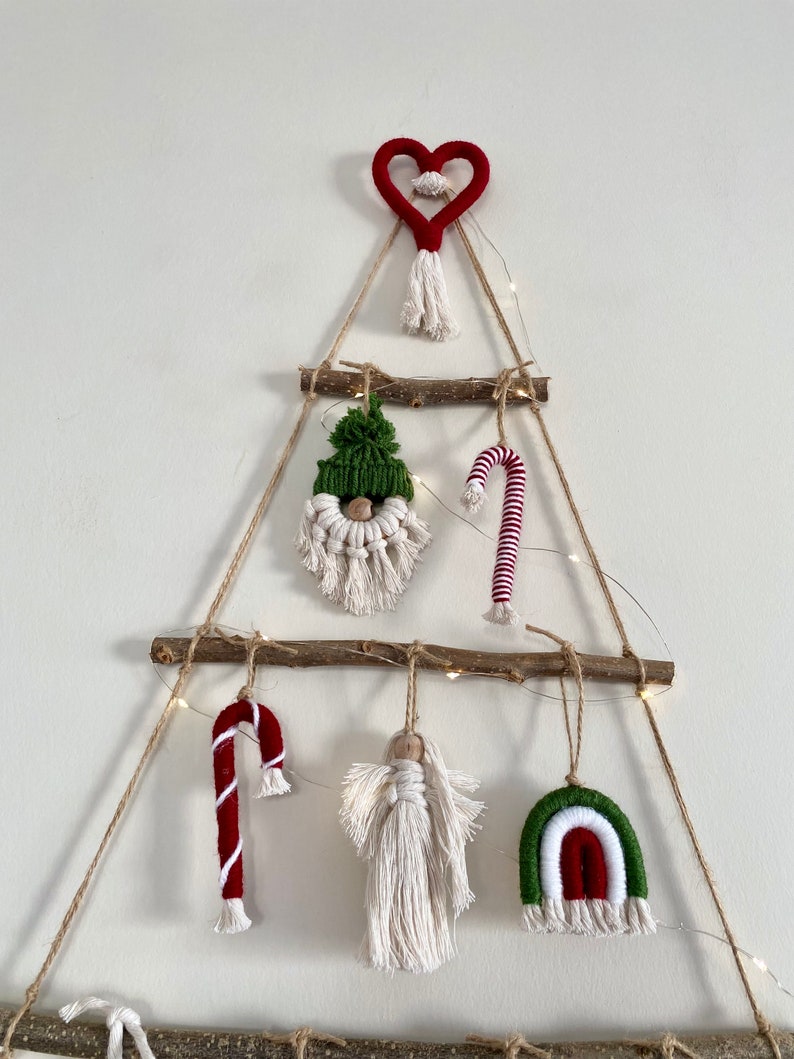 May include: A handmade Christmas tree wall hanging made of twine and wood. The tree is decorated with a red heart, a green and white gnome, a red and white candy cane, a white angel, and a green, white, and red rainbow.