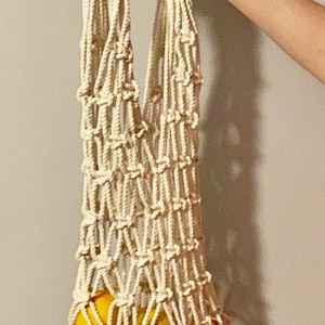May include: A white cotton string bag with four yellow oranges inside.