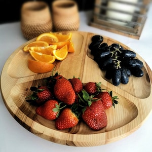 Könnte beinhalten: Ein Holztablett mit drei Fächern, gefüllt mit frischem Obst. Das Tablett ist aus hellem Holz und hat eine natürliche Oberfläche. Das Obst umfasst Orangenscheiben, Erdbeeren und Trauben.
