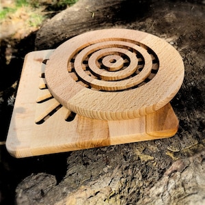 May include: A wooden cutting board with a circular design in the center. The board is made of light wood and has a natural finish.