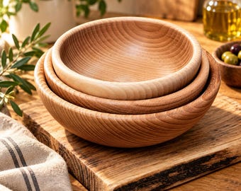 May include: A set of three nested wooden bowls with a smooth, light brown finish and visible natural wood grain patterns. The bowls are circular with rounded edges and are stacked one inside the other, showcasing a consistent light wood tone.
