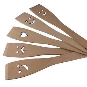 May include: Set of five wooden kitchen spatulas with different carved designs. Each spatula features a unique design, including a heart, a moustache, and smiley faces.