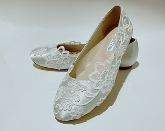 Op de afbeelding: Een paar lichtblauwe satijnen ballerina's met witte kant met bloemenmotief. De schoenen hebben een spitse neus en een platte hak.