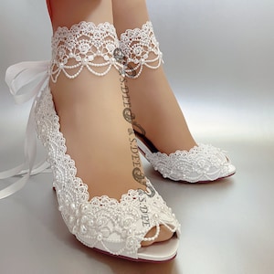 May include: White satin peep-toe heels with delicate lace and pearl embellishments. The shoes have a ribbon tie at the ankle.
