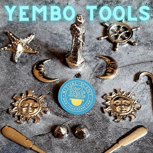 May include: An assortment of silver-toned ritual tools, including a starfish, crescent moons, suns with faces, a ship's wheel, a statue, and a curved cane. The image also features the text "YEMBO TOOLS" and a circular sticker with the text "RITUAL SCENT".