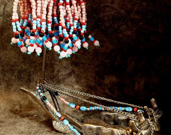 May include: A decorative metal sculpture featuring a beaded umbrella and a miniature ox-drawn cart. The umbrella has a gold-coloured top with pink, blue, and red beads. The cart and oxen are silver-coloured, with beaded accents in various colours.